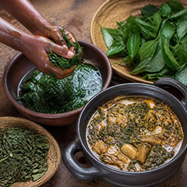 Washing fresh bitter leaf in a bowl beside a pot of bitter leaf soup