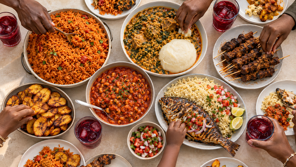 Festive West African family table with jollof, egusi, suya, plantain and attieke