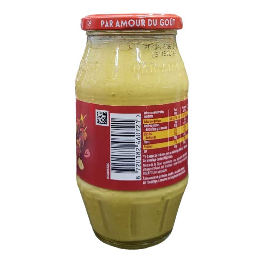 Jar of Amora Dijon Mustard (Moutarde de Dijon Fine & Forte) with red label and cap, displayed on a store counter with shelves of grocery items in the background.