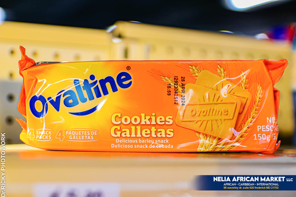 Package of Ovaltine Cookies (150 g) in bright orange packaging. The label features two rectangular cookies embossed with the “Ovaltine” logo, wheat graphics in the background, and text in English and Spanish reading “Cookies / Galletas.” The package highlights “4 snack packs” and the expiration date “18 JUL 2026.”