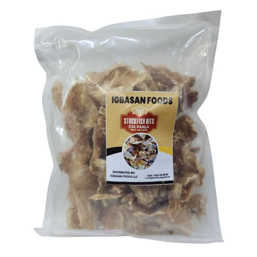 A clear resealable bag of Igbasan Foods Stockfish Bits (Eja Panla) showing dried fish pieces inside. The label is gold, white, and red, featuring the Igbasan Foods logo, product name, and “100% Natural” claim.