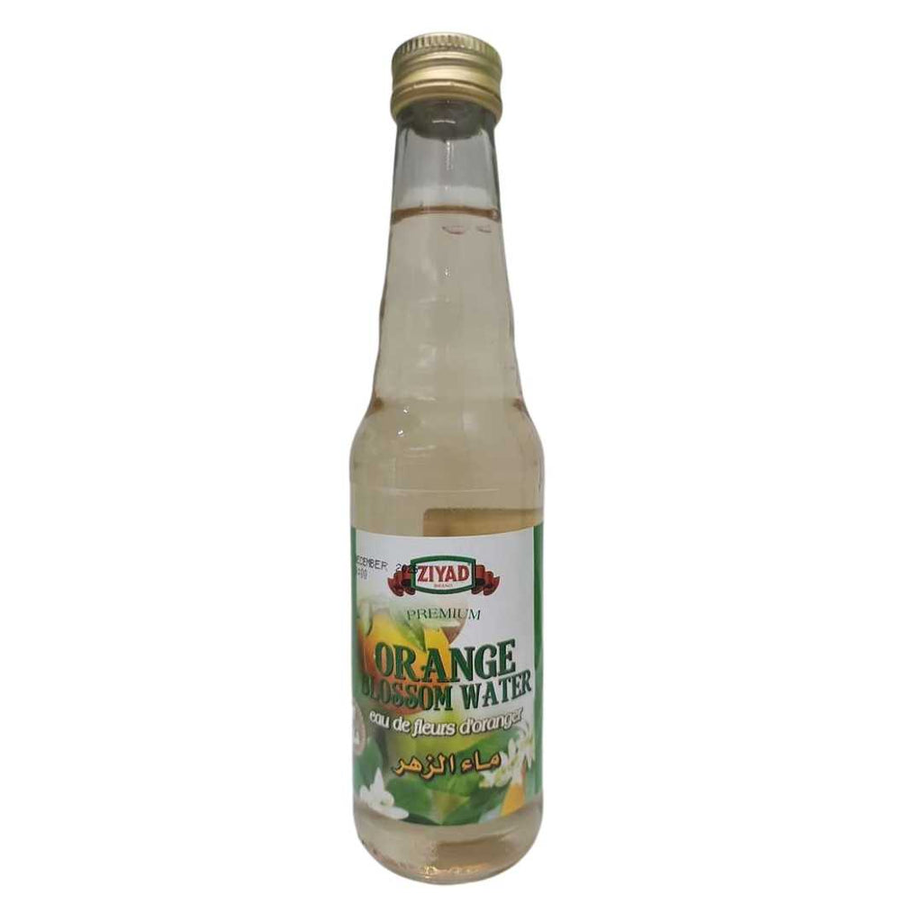 Bottle of Ziyad Premium Orange Blossom Water with a gold cap and clear liquid inside. The label shows white orange blossoms and a sliced orange, featuring the Ziyad logo and text in English, French (“eau de fleurs d’oranger”), and Arabic.